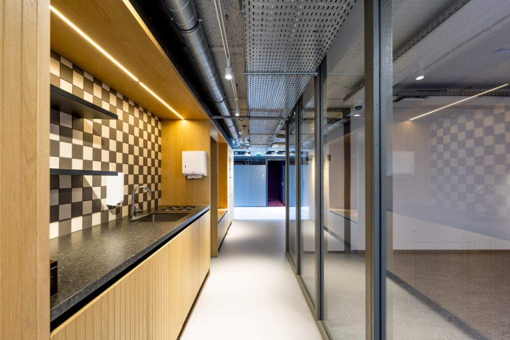 Modern kitchenette with checkered tile backsplash and wooden cabinetry in a hallway at Elizabeth Cady Stantonplein.